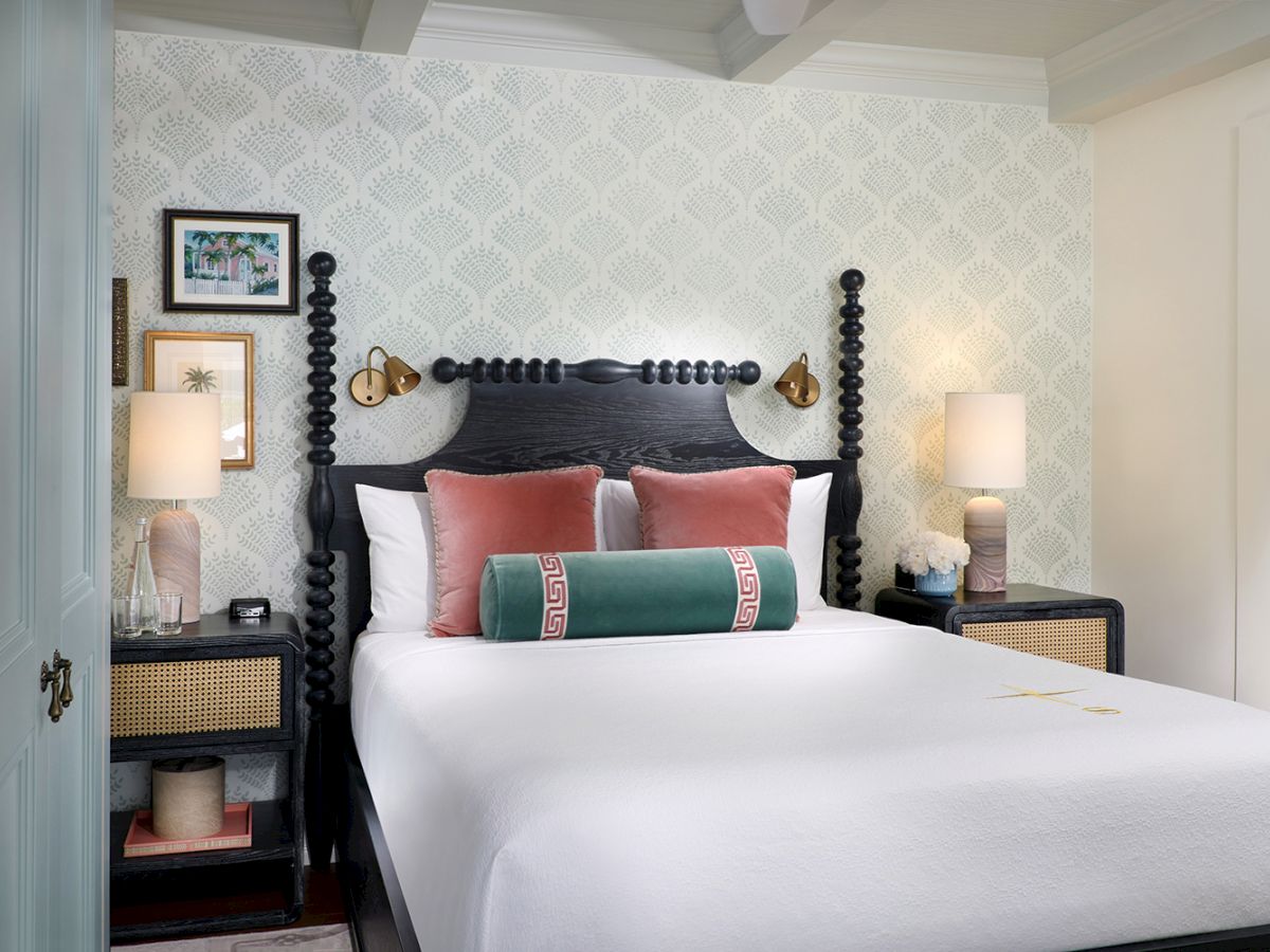 A stylish hotel bedroom with a carved headboard, white bed linens, pink and green pillows, and bedside lamps.