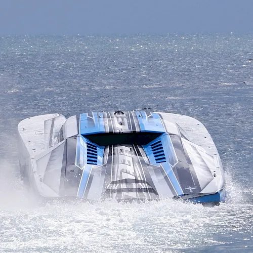 A high-speed futuristic racing boat skimming through choppy ocean water, throwing up a spray behind it.