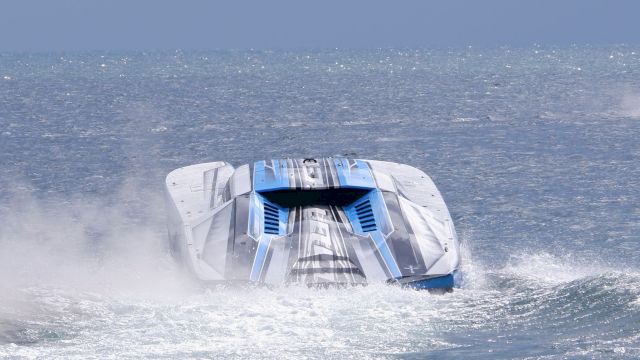 A high-speed futuristic racing boat skimming through choppy ocean water, throwing up a spray behind it.